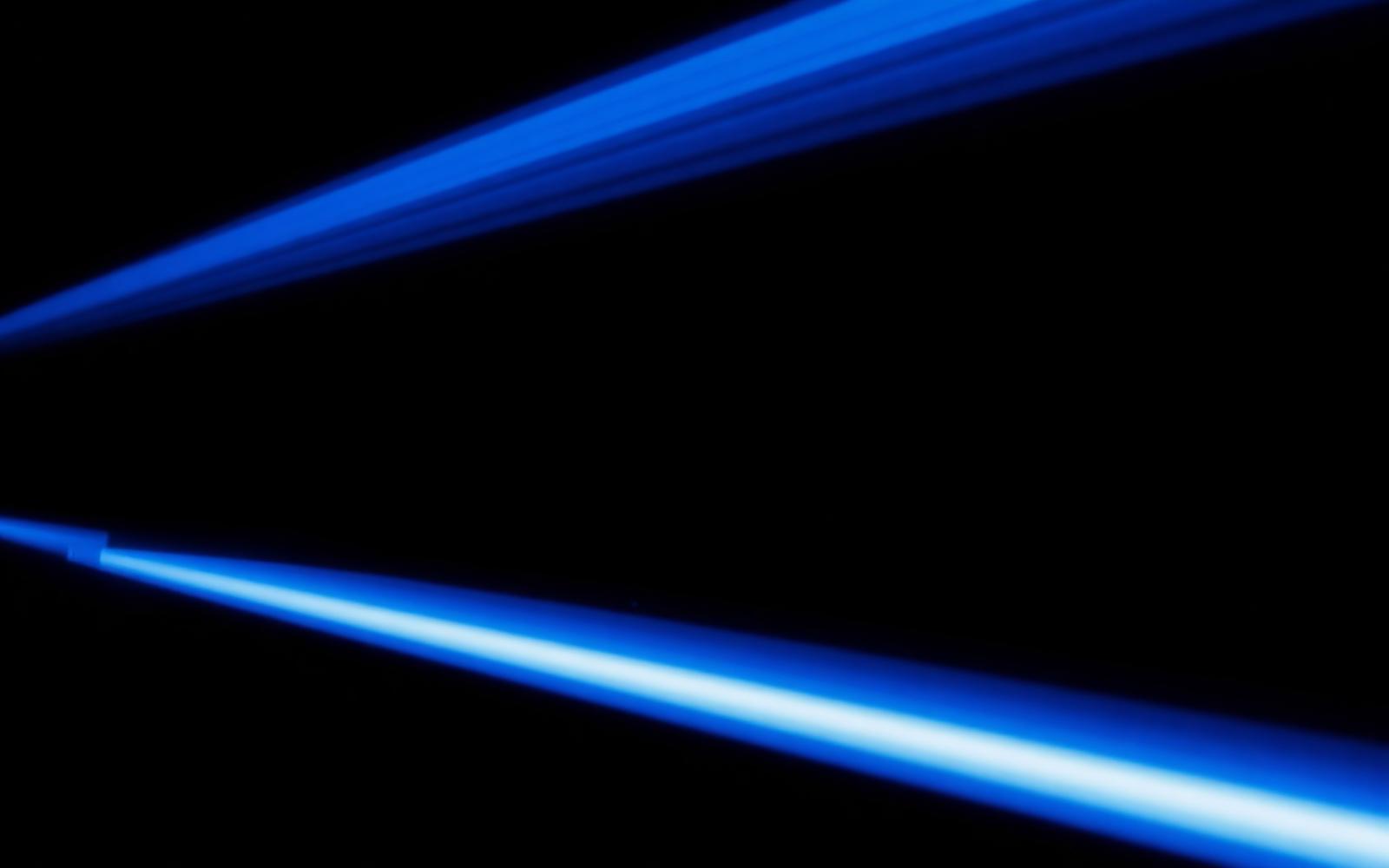Trazo abstracto de haces de luz láser sobre fondo negro.